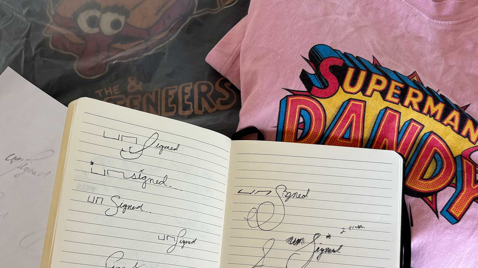 Unsigned Tees logo sketches in a notebook with shirts in the background